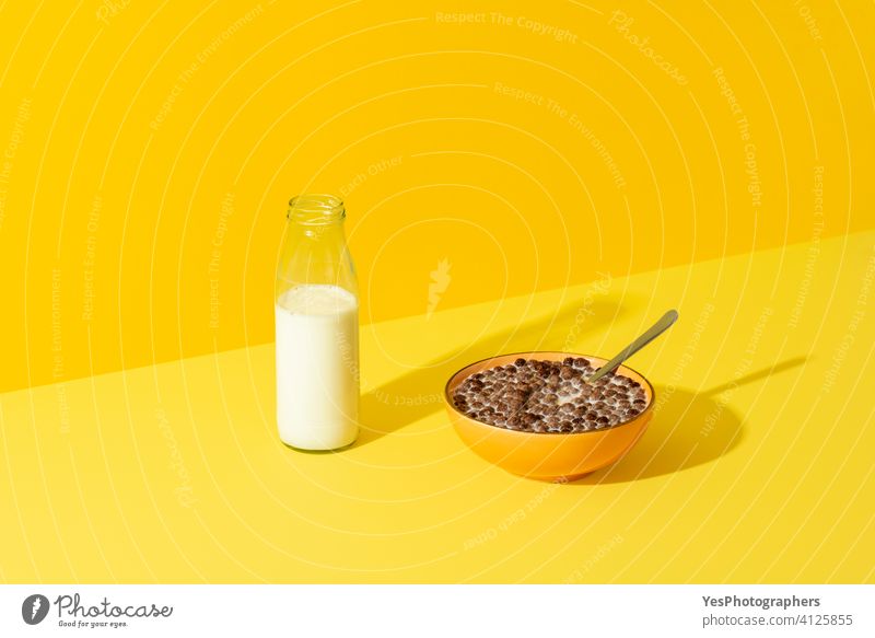 Chocolate cereals bowl and a bottle of milk isolated on a yellow background. abstract balls beverage black breakfast bright brown cereal bowl chocolate colorful