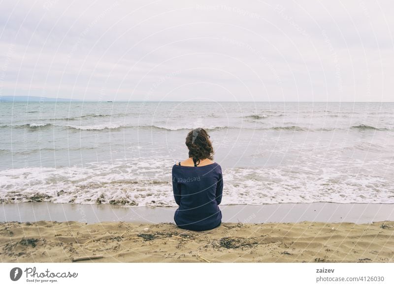 girl sitting on the sand on the shore of the beach looking at the horizon of the sea background travel copy space sad loneliness depression unhappy dream