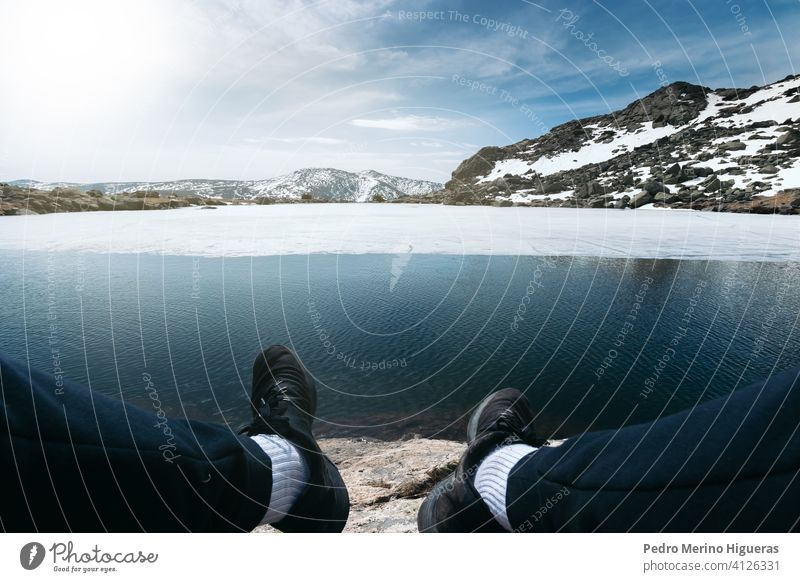Feet of a man sitting in front of a frozen lake in the top of a snowy mountain. Peñalara peak Madrid nature ice winter person leisure male travel hobby people