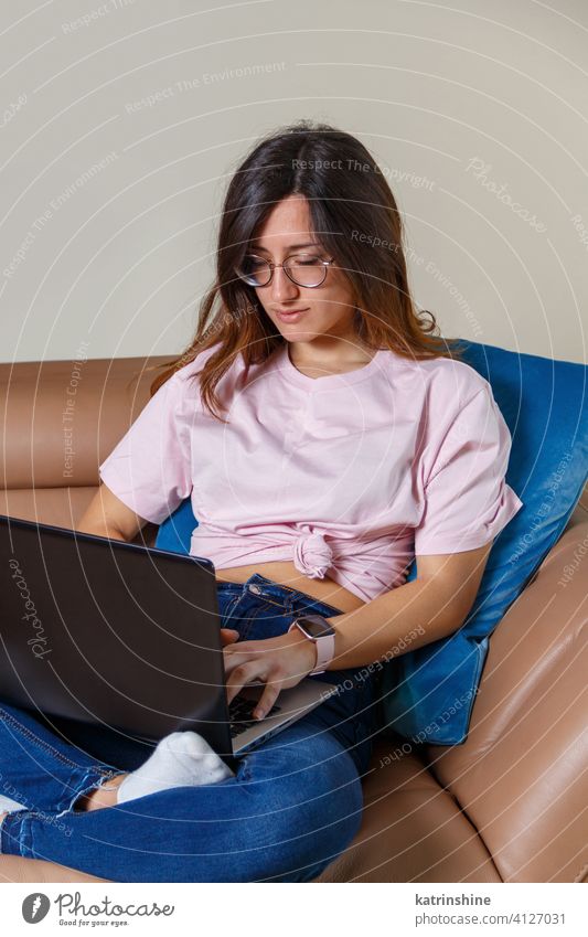 Young women working with laptop while sitting on the sofa at home wear mockup t-shirt learn student Lifestyle jeans serious concentrated indoor couch round neck