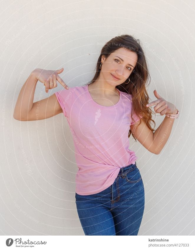 Young women wearing t-shirt and jeans point to the center of a t-shirt mockup pink smile roundneck casual mock up alone slim long hair Person Outdoor wall