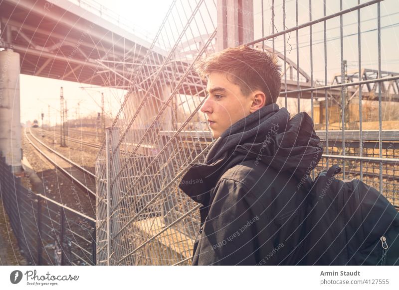 Serious young man with backpack on travel, the railroad in the background tracks rucksack landscape outdoors serious confident tired railway alone journey