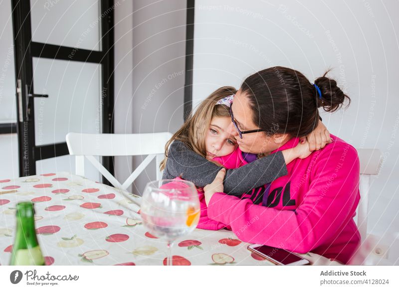 Upset daughter hugging mother at home upset support console calm love casual table sit girl woman child kid parent glasses problem lifestyle relationship