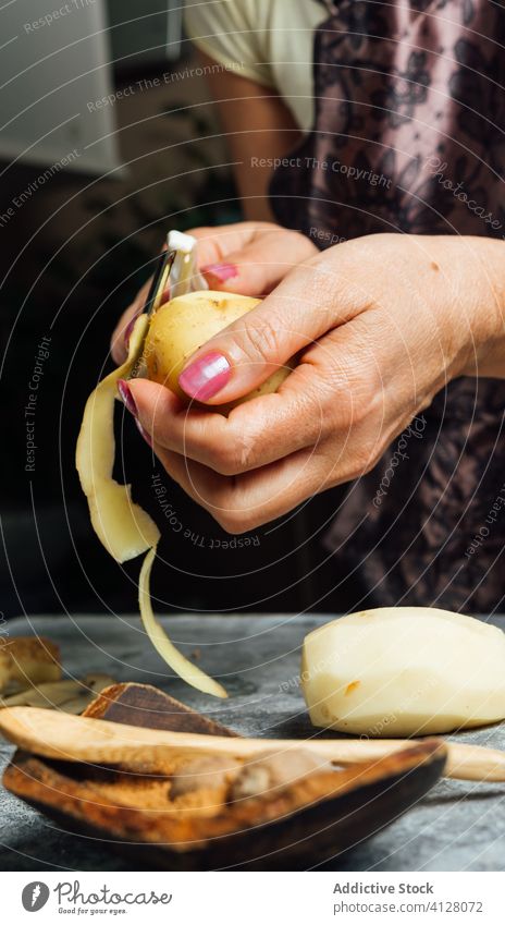 Crop woman peeling potato in kitchen peeler housewife vegetable cook dinner raw prepare female process fresh stand food uncooked cuisine culinary nutrition