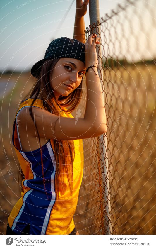 Sensual young lady standing near metal fence on street woman sportswear cool generation modern style urban sporty uniform cap baseball city slim fit rest