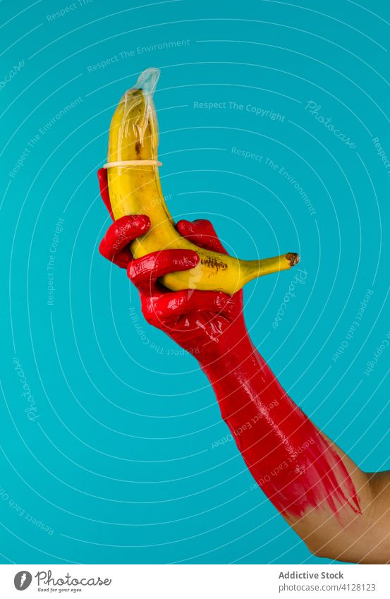 Condom on banana in hand of crop person condom paint latex fresh show fruit safe sex period hiv concept rubber colorful contraception protect safety prevent