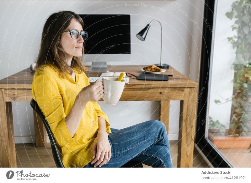 Thoughtful woman drinking coffee and looking out window thoughtful rest telework break beverage computer freelance relax keyboard interior dreamy monitor
