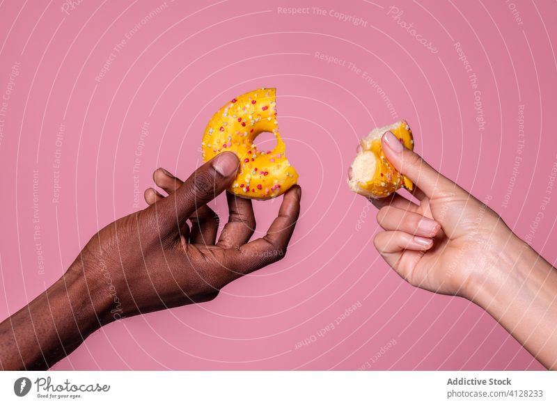 Crop multiracial hands holding bitten doughnut on pink background sweet couple tasty food delicious dessert snack pastry bakery culinary gourmet meal leisure