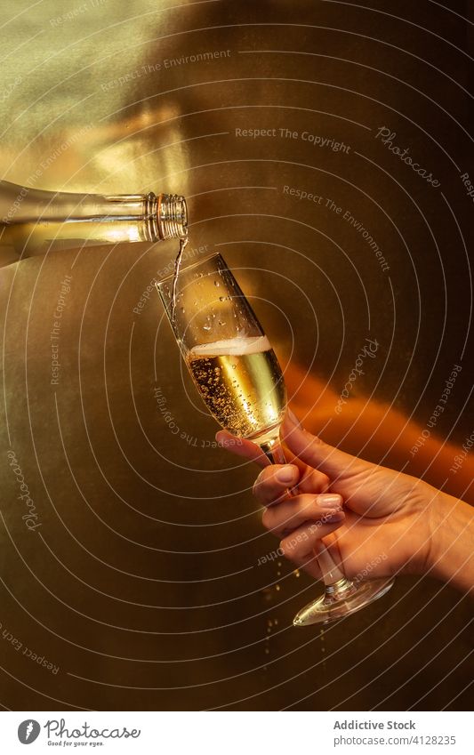 Anonymous person pouring champagne from bottle into glass on golden background hand hold wineglass alcohol celebrate drink holiday event body part sparkle