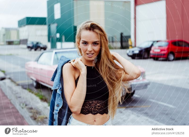 Attractive blonde girl standing on the sidewalk and messing with her hair woman young braids sitting pink car classic old grunge summer portrait leisure urban