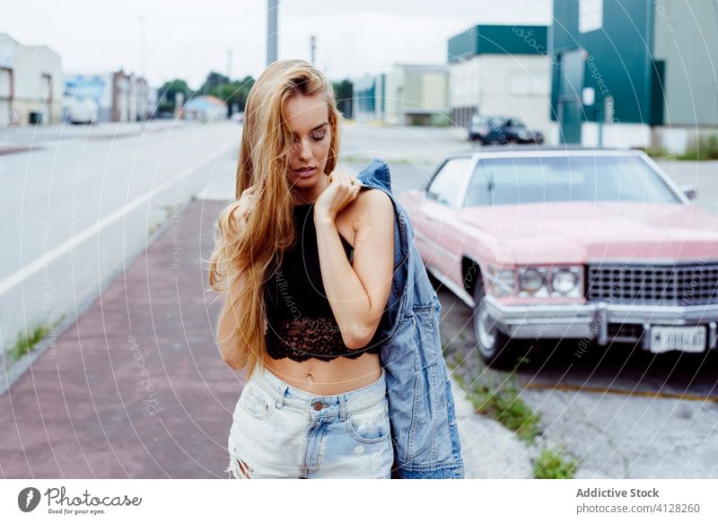 Attractive blonde girl standing on the sidewalk and messing with her hair woman young braids sitting pink car classic old grunge summer portrait leisure urban