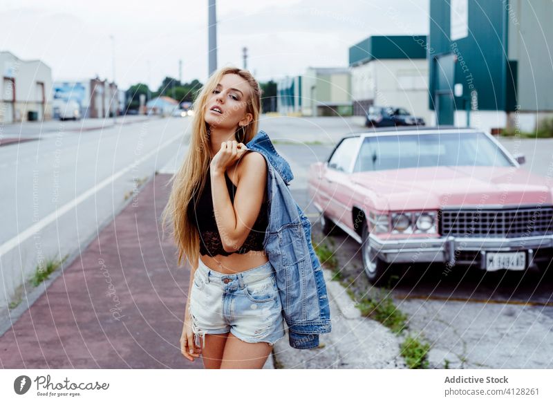 Sensual blonde girl standing on the sidewalk looking at the camera woman young braids sitting pink car classic old grunge summer portrait leisure urban city