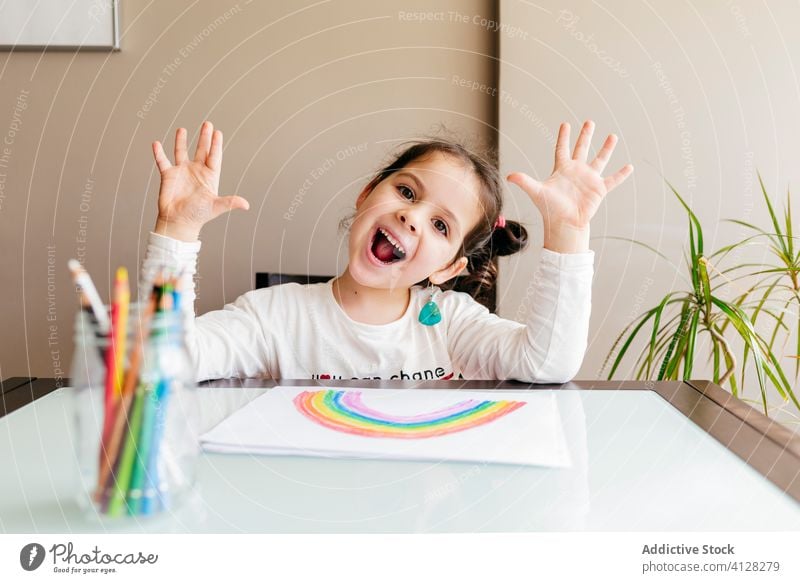 Cheerful little girl looking at camera while drawing at home positive fun painter hand up palm playful grimace make face adorable content rainbow kid creative