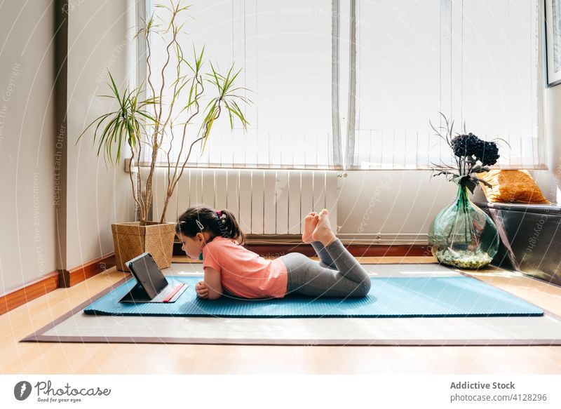 Little girl resting after yoga in light room kid mat video tablet lying down tutorial practice at home stress relief watch harmony spirit internet online device