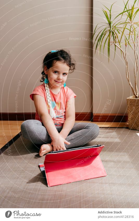 Little girl resting after yoga in light room kid mat video tablet sit tutorial practice at home stress relief watch focus harmony spirit internet online device