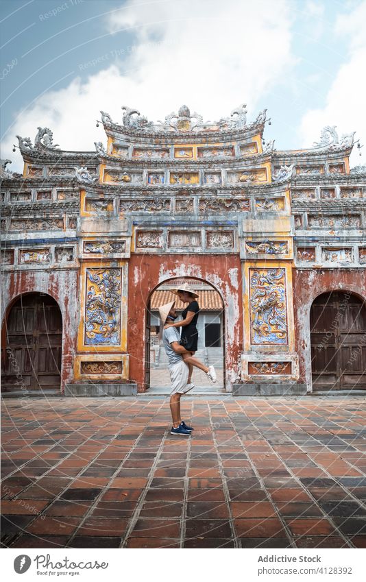 Delighted traveling couple near arch of Buddhist temple buddhism lift boyfriend girlfriend vacation summer vietnam asia pagoda in love tourist holiday traveler