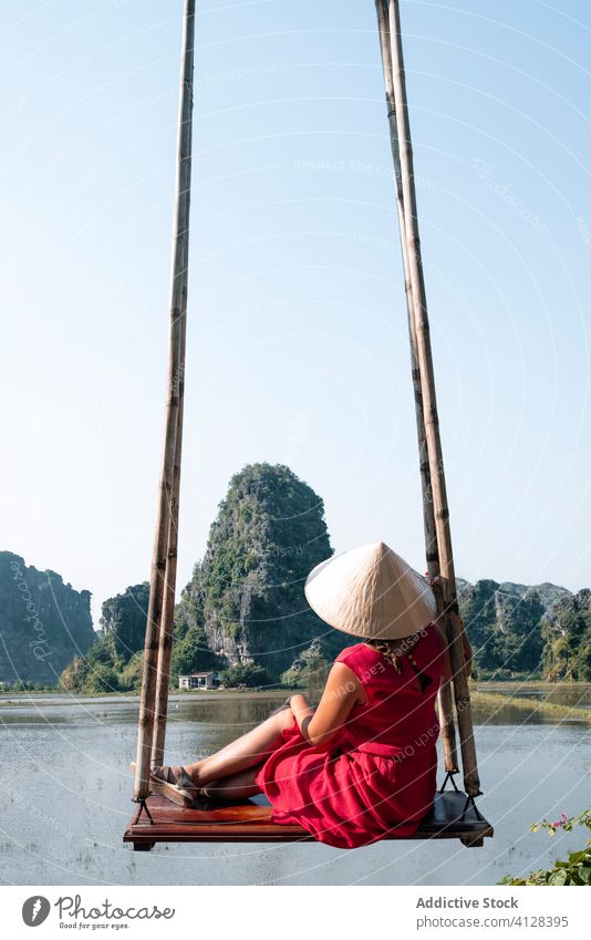 Traveling woman on swing near lake tourist scenery amazing admire travel water rock vietnam asia tourism traveler conical hat tradition oriental casual outfit
