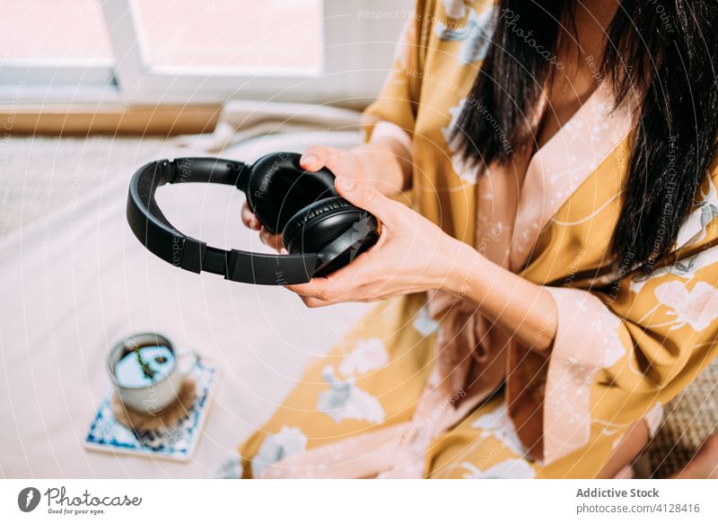 Anonymous woman picking up music headphones mat chill home robe tea zen sensual social media weekend floor sleepwear taking using gadget drink rest online cozy