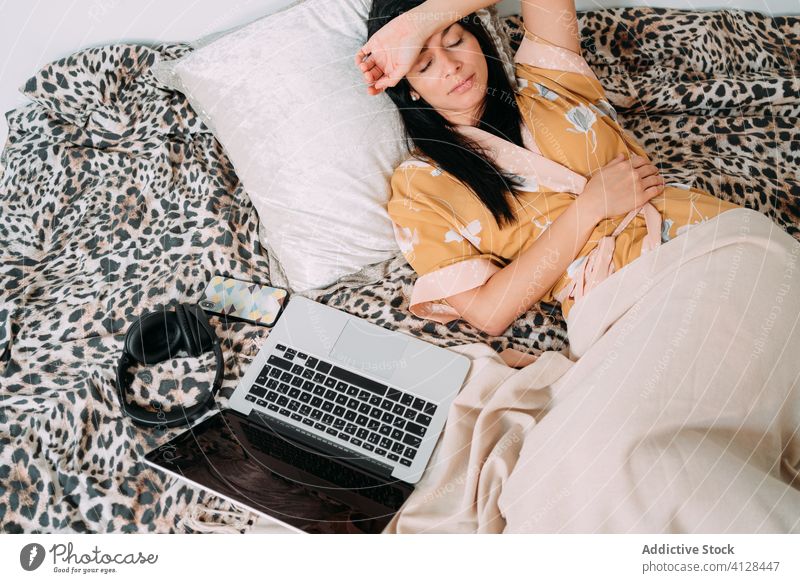 Woman resting close to laptop and headphones on bed woman music listen chill happy enjoy comfort lounge bedroom relax lifestyle gadget smartphone device home