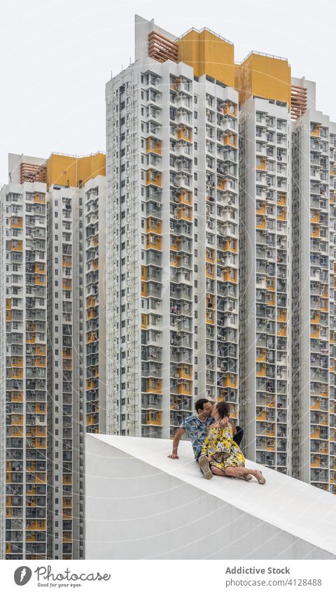 Couple kissing on sloping roof against high rise buildings in Hong Kong couple skyscraper residential height love having fun slope multistory facade district