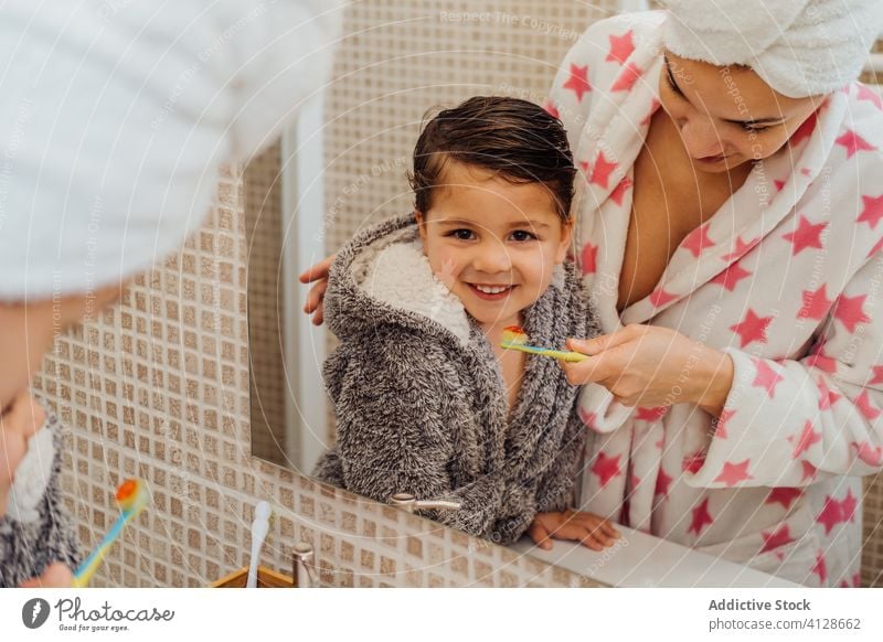 Cheerful son and mother with toothbrush in bathroom teeth boy bathrobe oral hygiene smile little child mom parenthood healthy mirror kid wet hair dental care