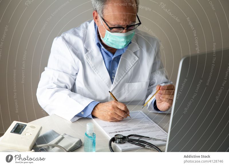 Aged male doctor filling medical report after examination of patient man aged thermometer temperature virus infection practitioner diagnosis quarantine