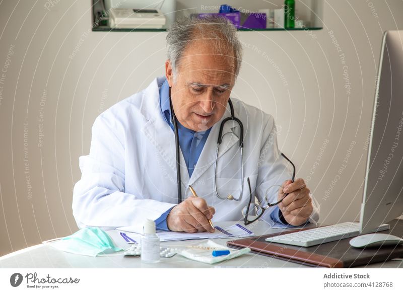 Aged male doctor filling medical report after examination of patient man aged virus infection practitioner diagnosis quarantine take note senior elderly