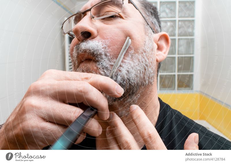 Bearded man shaving with straight razor beard mature bathroom procedure hygiene grooming classic knife vintage care male middle age routine careful sharp treat