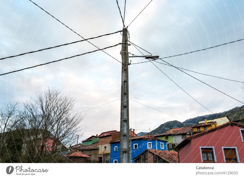 Streetlight, power lines, a colorful village, bare trees on a winter morning. Street lighting power cable Electricity pylon street lamp Energy stream