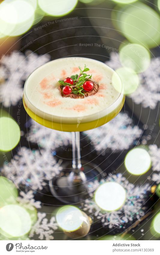 Vertical photo of a round glass of mezcal cocktail with kiwi and maple syrup with table decorated with snow stars presentation shape decoration plastic mexico