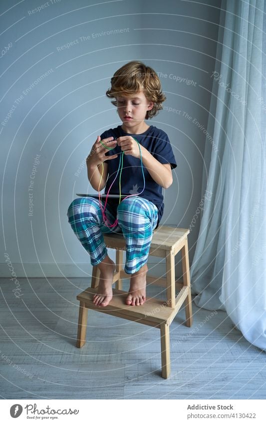 Child with tablet learning cats cradle game kid string play creativity figure stool pajamas home boy focus preteen tie imagination skill develop finger device