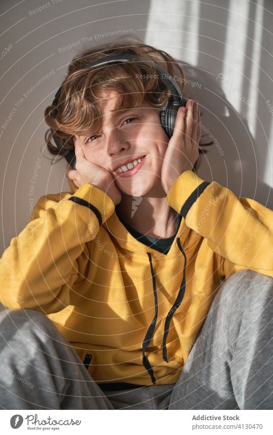 Happy carefree small boy in headphones enjoying favorite music in light contemporary room alone dream song listen relax music lover lounge kid chill child home
