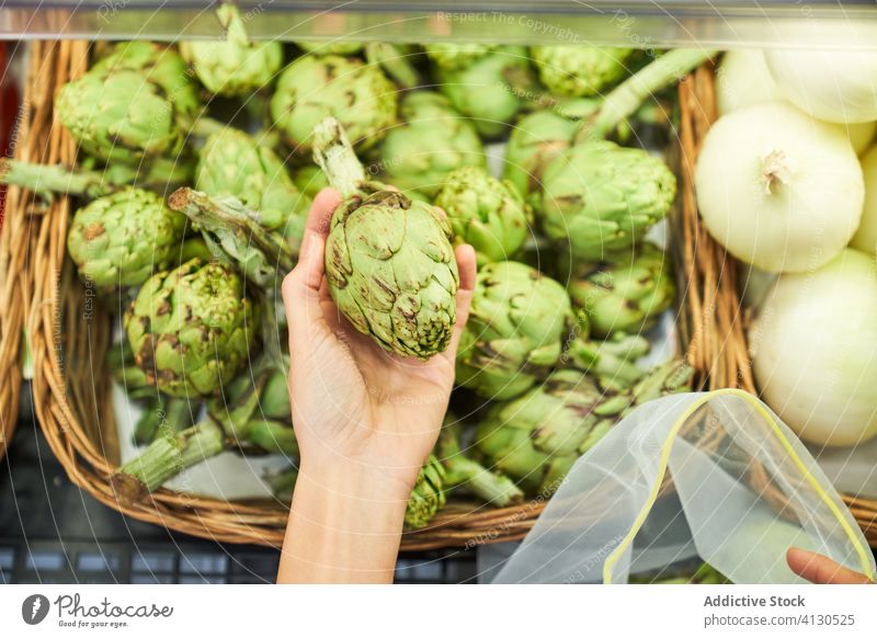Female hand picking up artichokes from a basket with reusable bag food green ripe fresh vegetable harvest raw organic plant stand stall exotic closeup variation