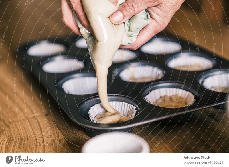 Senior housewife pouring dough in muffin cases fill tray batter kitchen senior female home confectioner cook prepare paper liner muffin liner cupcake liner