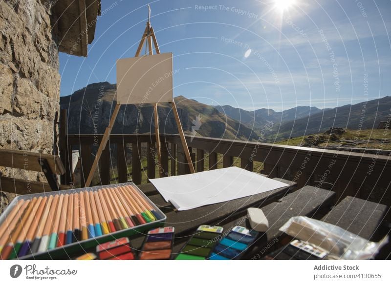Easel with canvas and drawing equipment on wooden terrace in sunny mountain of Cantabria inspiration easel art pain table old stone house tool nature sunlight