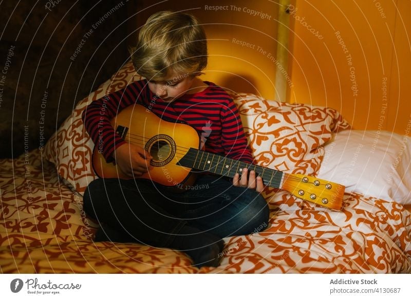 Calm boy playing guitar on bed ukulele child chill comfort having fun hobby cantabria spain kid childhood casual outfit sit relax rest concentrate focus calm