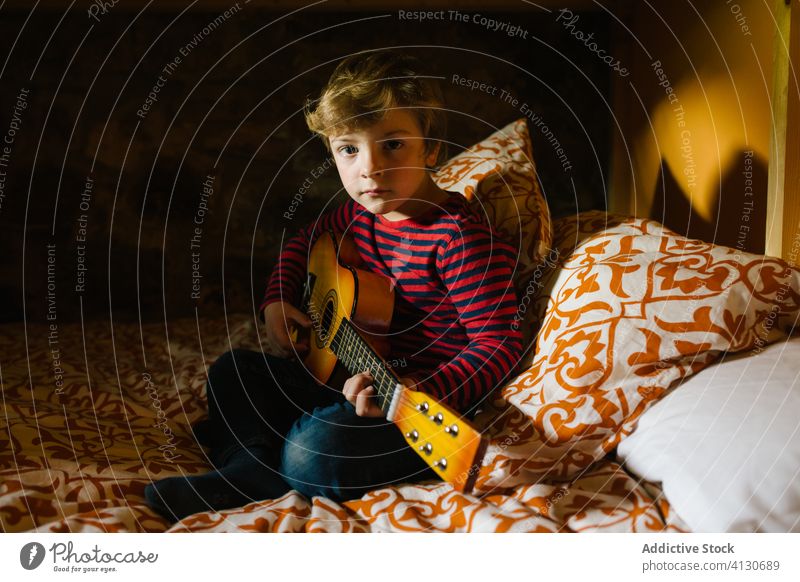 Calm boy playing guitar on bed ukulele child chill comfort having fun hobby cantabria spain kid childhood casual outfit sit relax rest concentrate focus calm