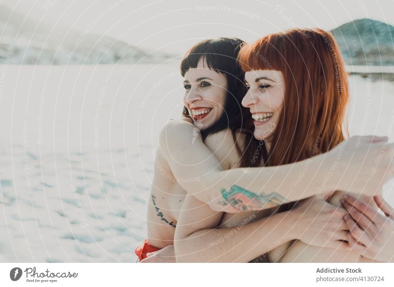Happy embracing women sitting on snow happy together embrace girlfriend topless freedom close laugh smile hug bonding delight affection romantic enjoy couple