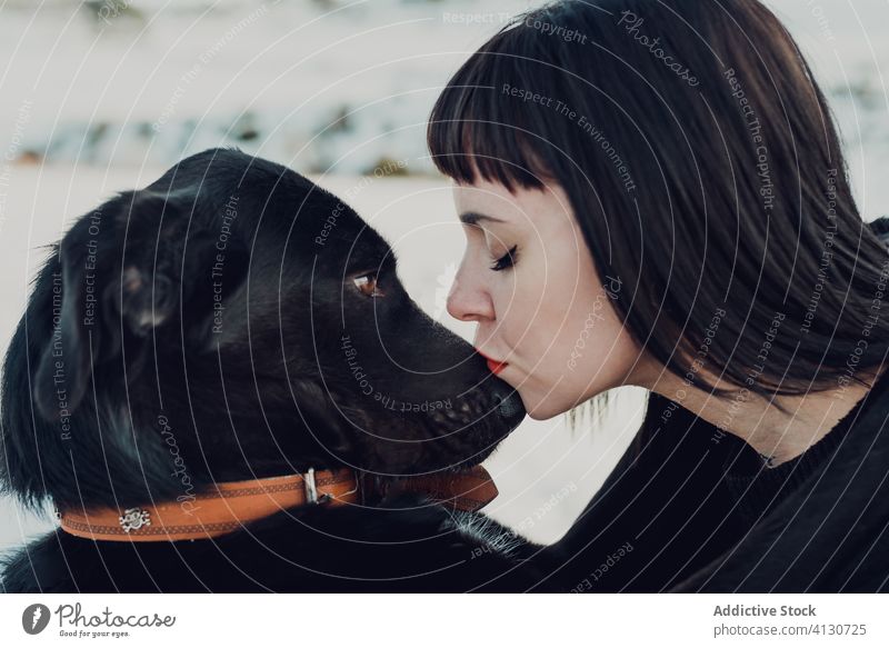 Young woman kissing black dog pet together love friend companion adorable animal canine domestic purebred cute female young brunette affection friendship loyal