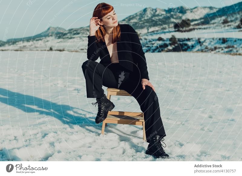 Trendy woman in black suit sitting in snowy field trendy style fashion confident modern nature bare chest female independent formal lady young elegant outfit