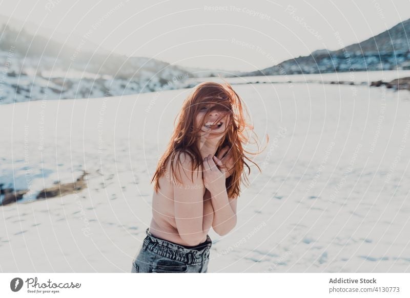 Young woman with red hair standing in snowy field topless winter flying hair nature happy relax wind female bare shoulders valley enjoy naked long hair