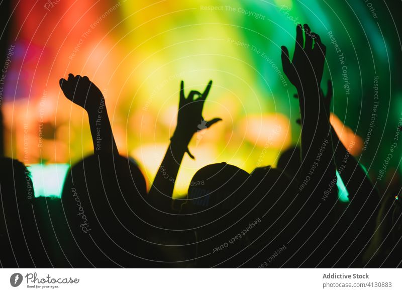 People with raised arms during show concert perform crowd people audience arms raised silhouette stage illuminate neon music event entertain light night