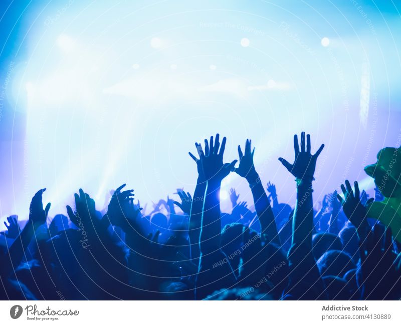 People with raised arms during show concert perform crowd people audience arms raised silhouette stage illuminate blue neon music event entertain light night
