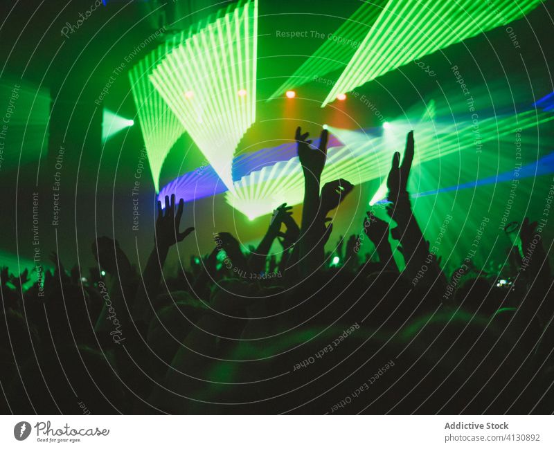 People with raised arms during show concert perform crowd people audience arms raised silhouette stage illuminate blue green neon music event entertain light