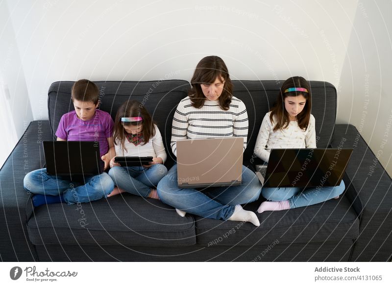 Serious mother and kids spending time together using gadgets on sofa at home children laptop busy addict browsing woman leisure separate sibling parent internet