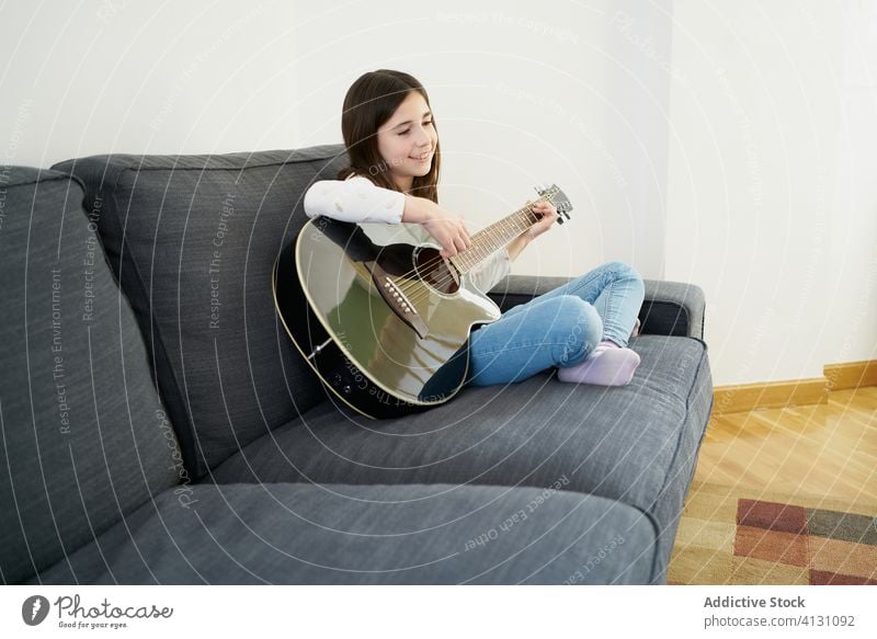 Young girl learning sister to play guitar on sofa at home children together teach explain sibling acoustic hobby sit kid leisure music relax living room melody