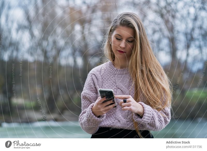 Young woman browsing smartphone while resting in park at sunset happy cheerful glad using watching social media stone bench recline smile internet online