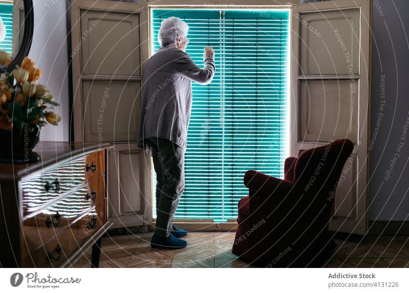 Senior woman looking out window during coronavirus quarantine stay home senior lonely mask prevent old female protect alone solitude aged infection problem