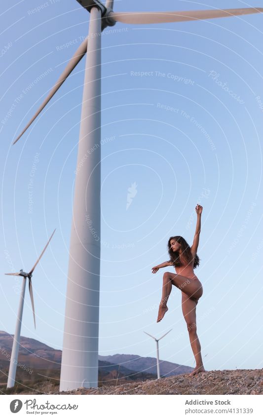 Young slim lady dancing under windmill on sunny day woman bodysuit dance harmony flexible ecology nature environment alone hand up perform balance alternative