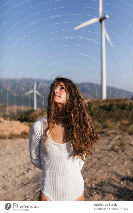 Tender female standing alone near wind farm on sunny field woman countryside sensual nature ecology slim style alternative windmill energy move model flexible